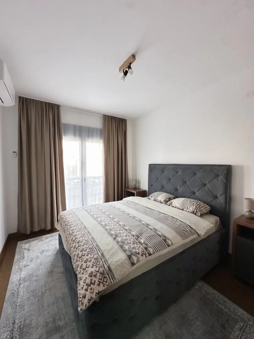 Furnished bedroom with a double bed and a window with curtains.