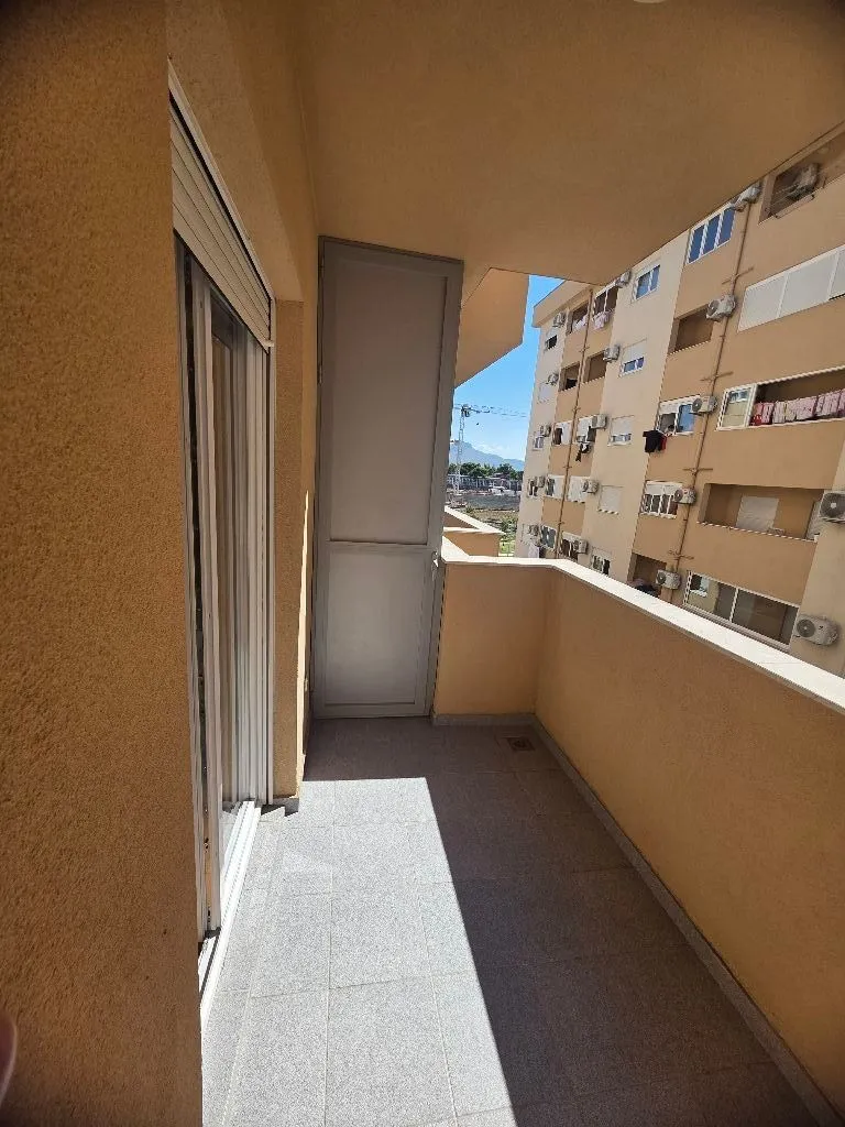 Prostrana terasa sa pločicama i pogledom na okolne zgrade.