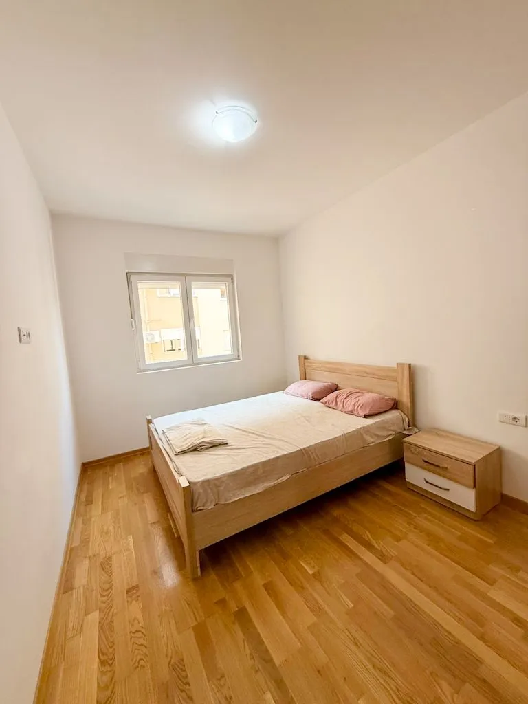 Svjetla spavaća soba sa drvenim krevetom i noćnim stolićem.