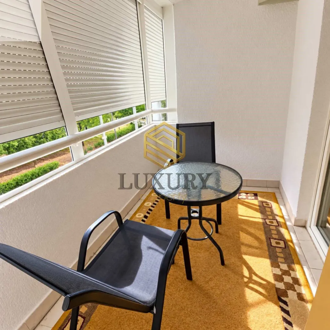 Enclosed balcony with seating furniture and a view of greenery.