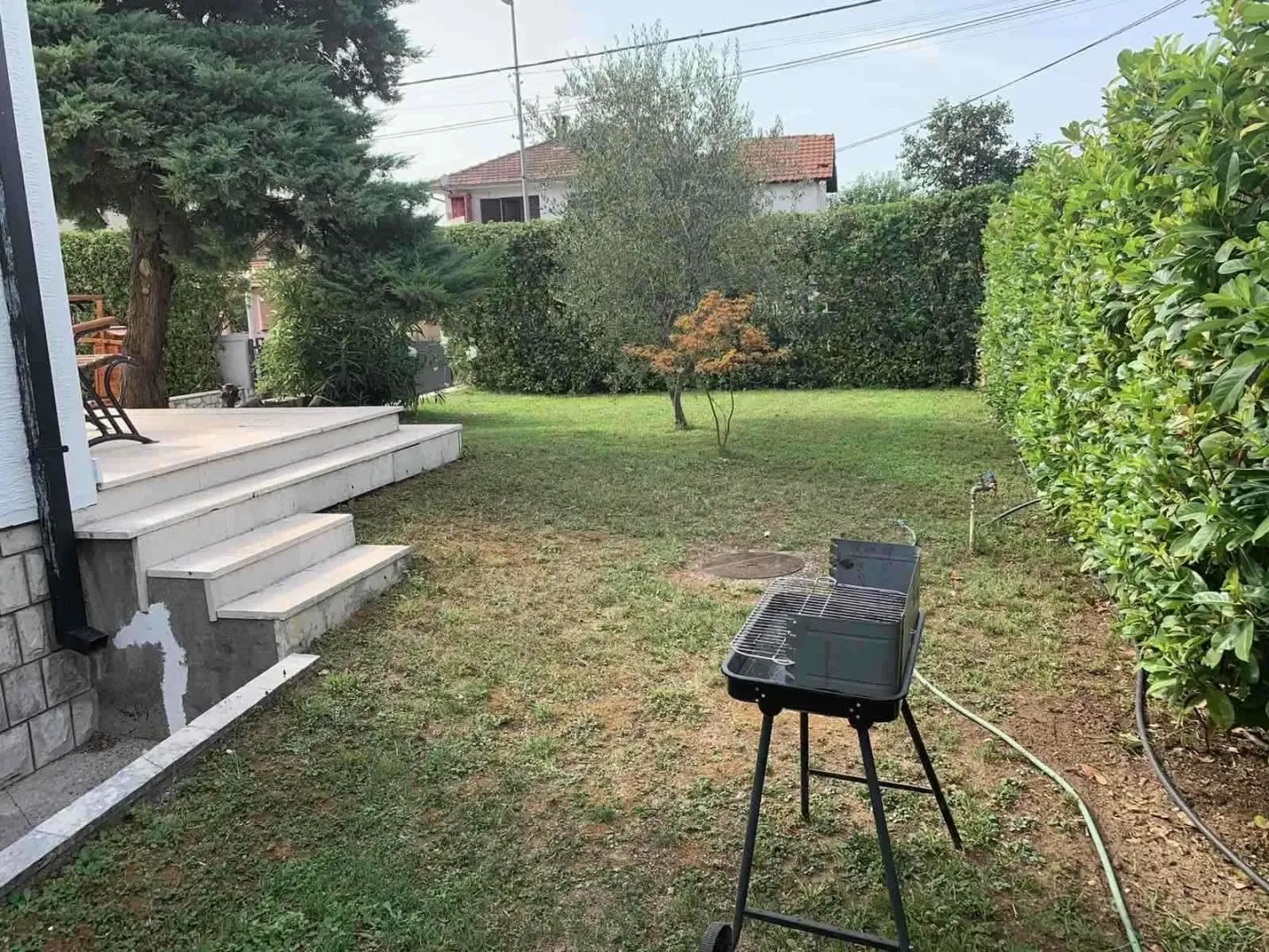 A landscaped yard with a lawn and a barbecue grill next to the house.