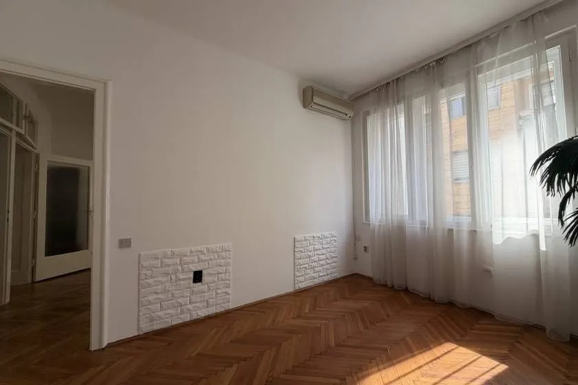 Empty room with parquet flooring and large windows.