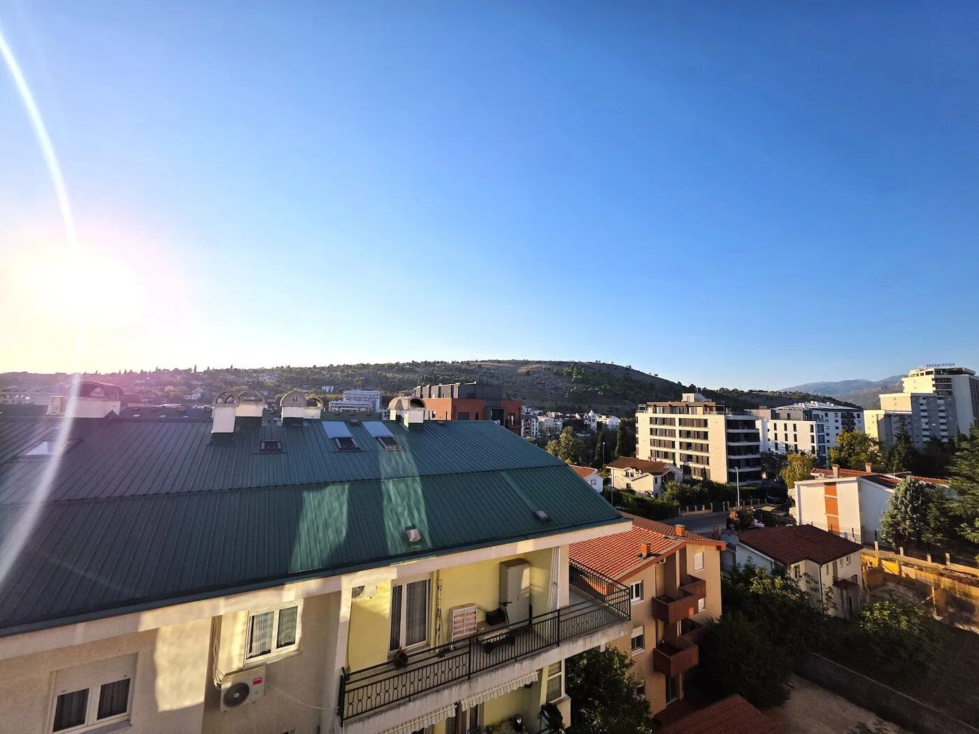 View from the terrace towards surrounding buildings and a hill in the background.