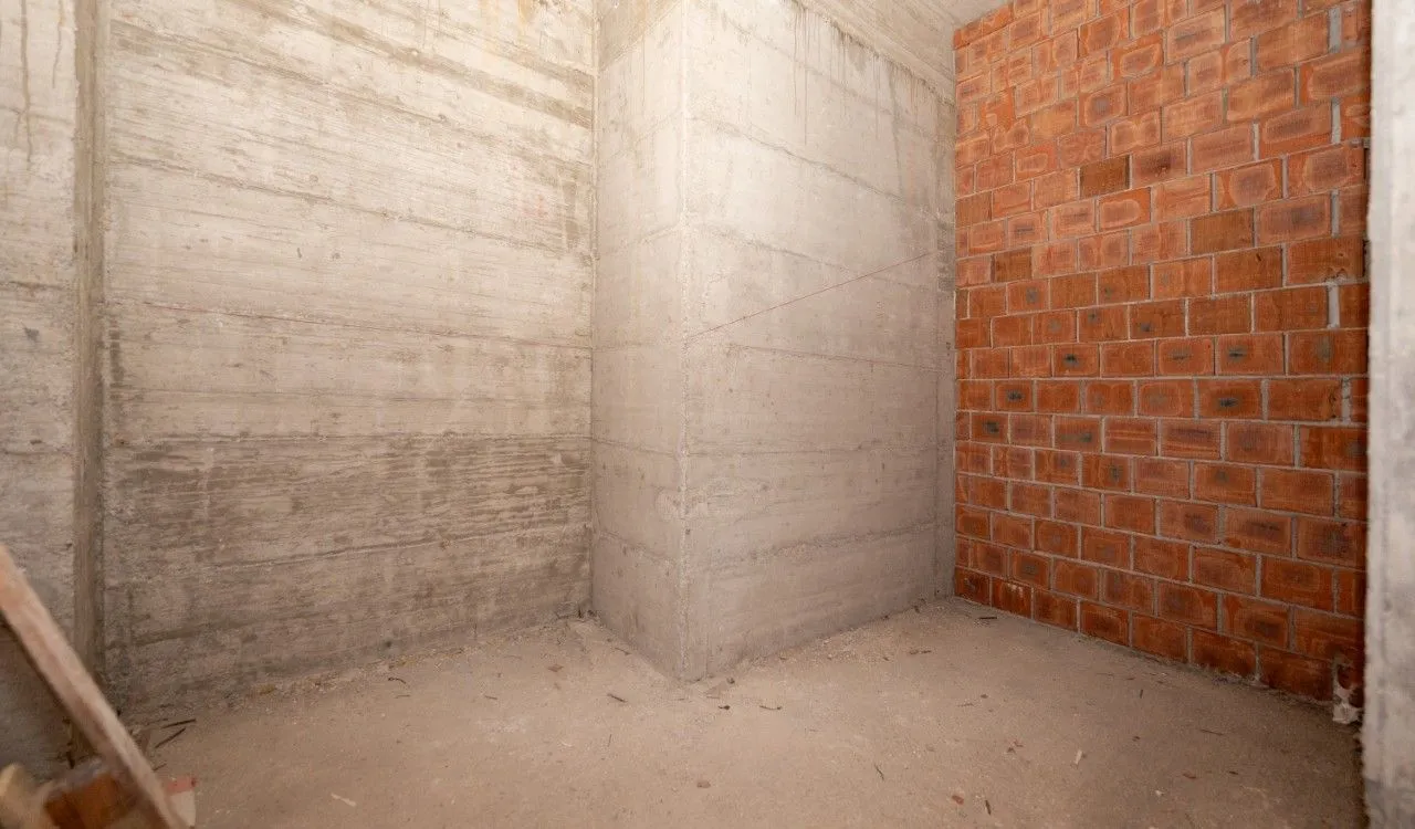 Unfinished room in grey phase with concrete and brick walls.