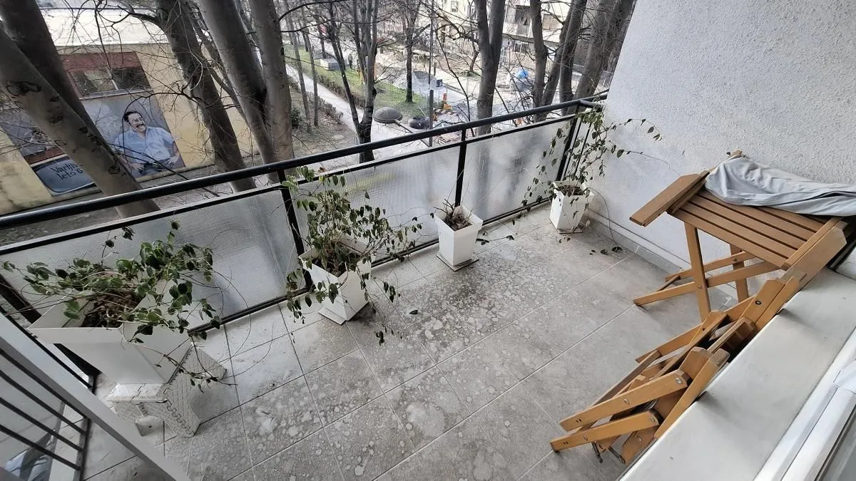 Manji balkon sa keramičkim pločicama, saksijama i drvenim sklopivim stolom.