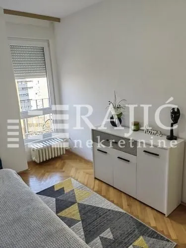 Small lit bedroom with a white dresser and a rug.