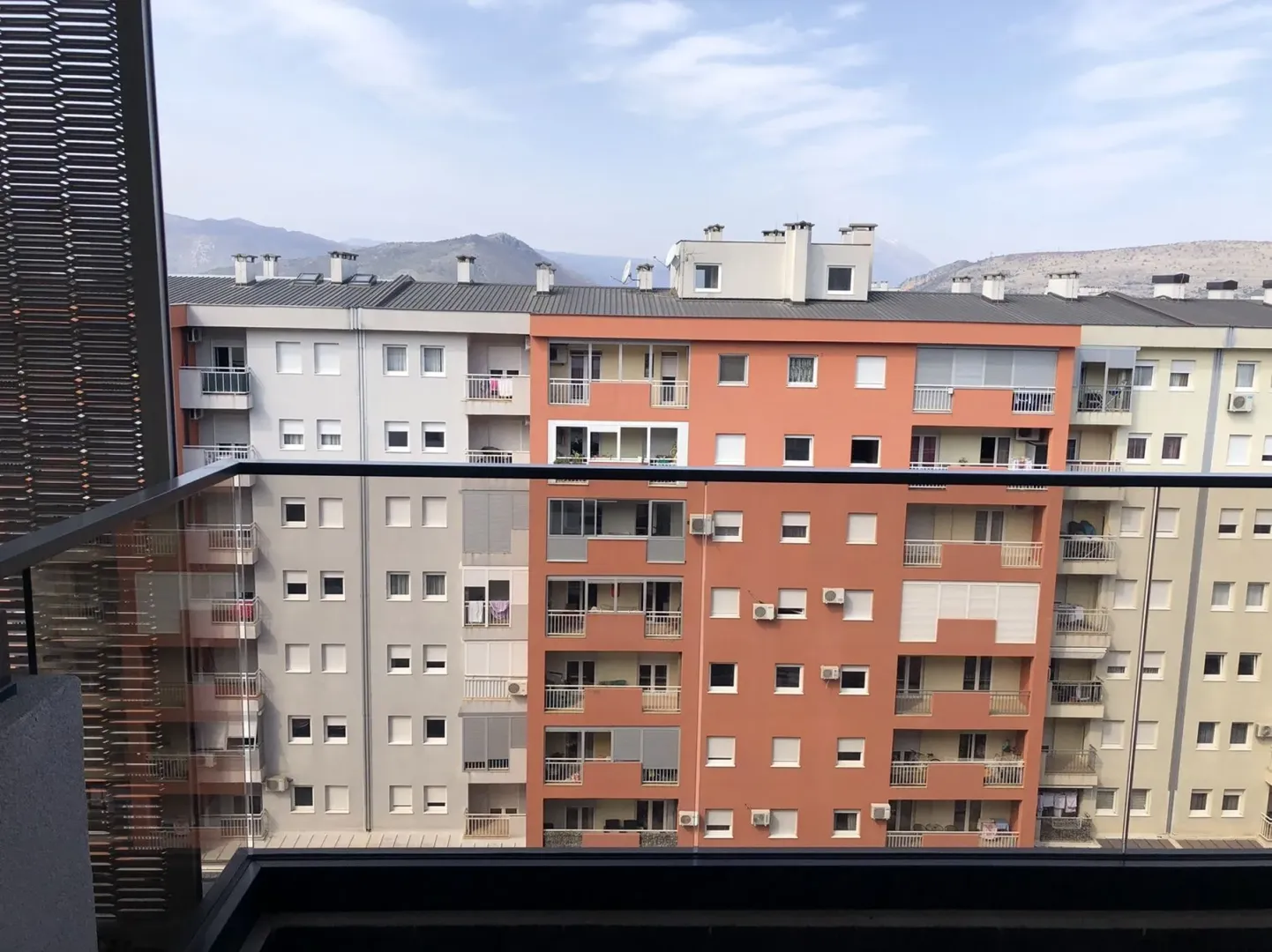 View from the balcony overlooking nearby residential buildings and distant mountains.