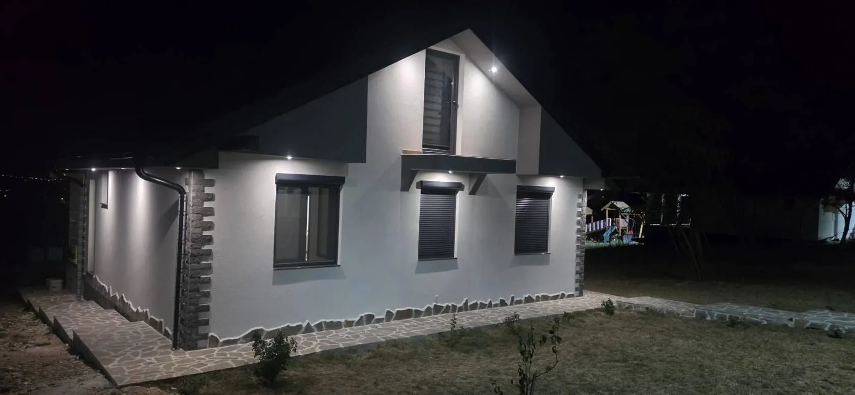Noćni pogled na osvetljenu fasadu i dvorište kuće.