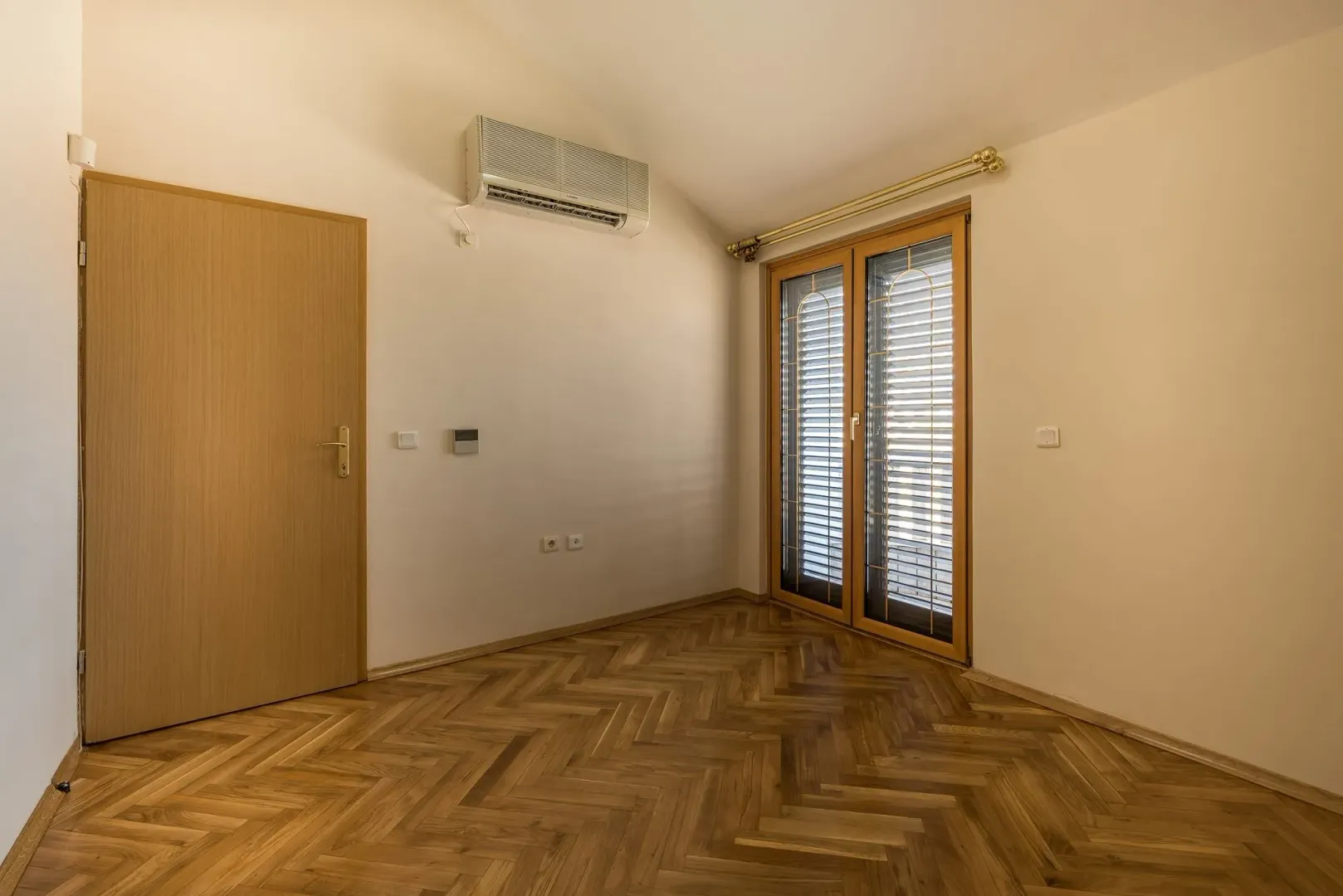 An empty bright room with parquet flooring and air conditioning.