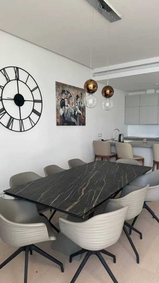 Moderna trpezarija sa velikim stolom i stolicama, povezana sa kuhinjom.