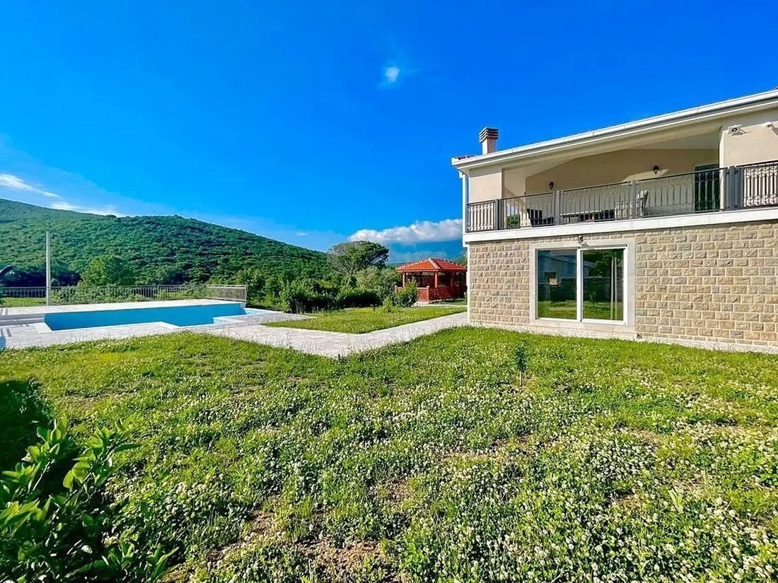 Pogled na dvorište kuće sa bazenom i zelenom površinom.