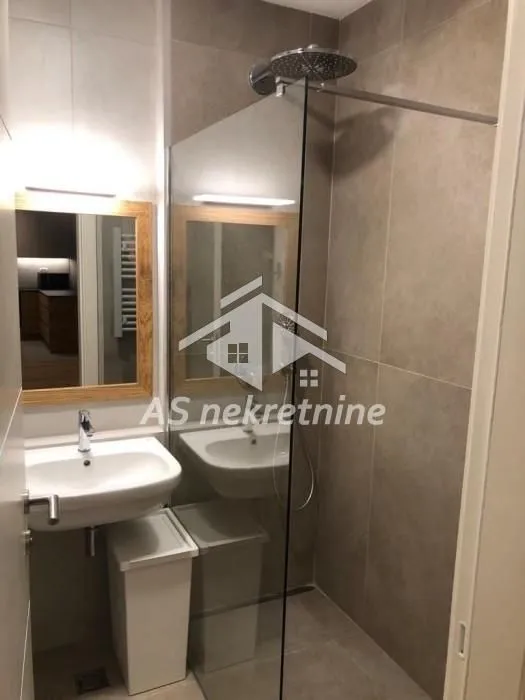 Manje kupatilo sa tuš kabinom, umivaonikom i ogledalom.