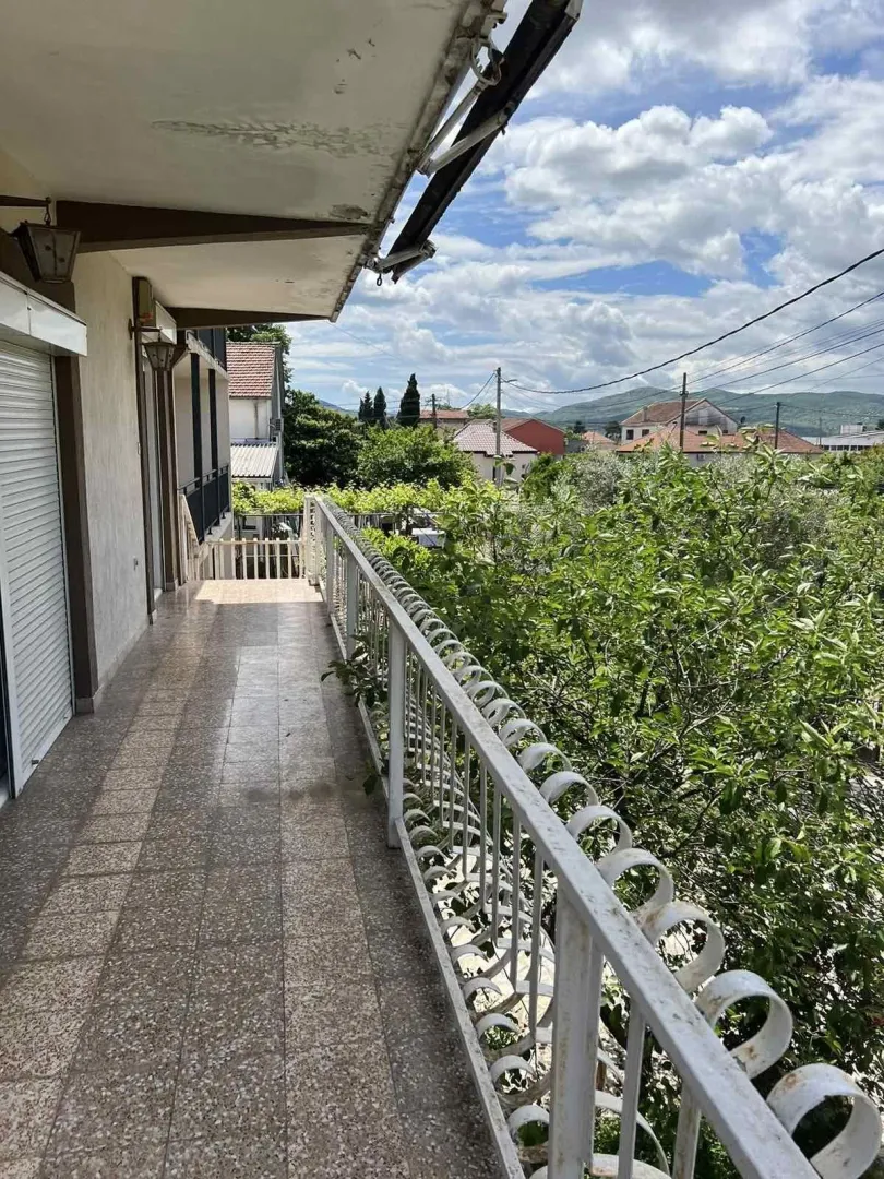 Long covered balcony with a metal railing and a view of greenery and surrounding houses.
