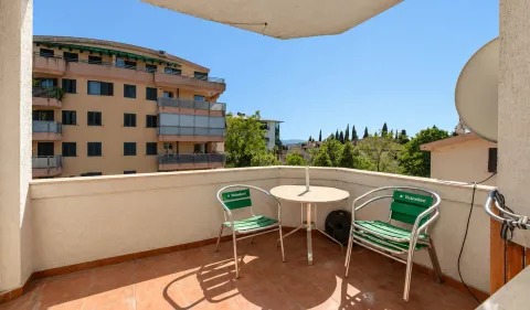 Furnished balcony with a table and two chairs overlooking surrounding buildings and greenery. - image 13