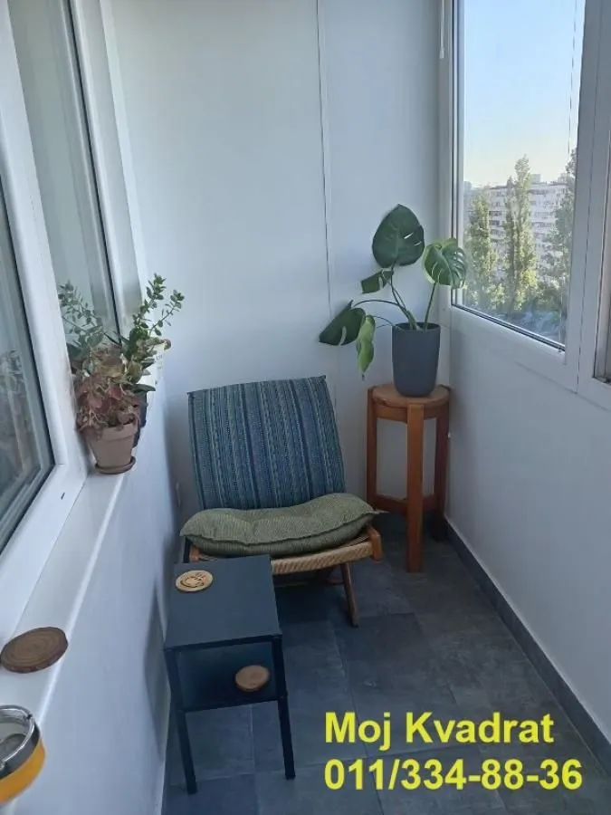 Enclosed balcony with an armchair, small table, and houseplants.