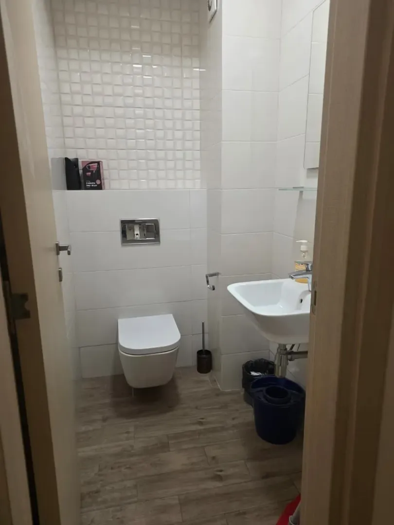 Small bathroom with white tiles, a washbasin and a toilet bowl.
