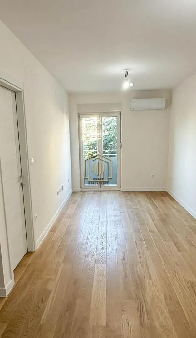 Prazna soba sa parketom, klima uređajem i balkonskim vratima.