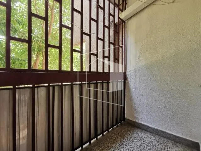 Natkrivena terasa sa metalnom ogradom i pogledom na zelenilo.