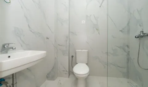 Savremeno opremljeno kupatilo sa bijelim mermernim pločicama, umivaonikom, WC šoljom i tuš kabinom. - image 6