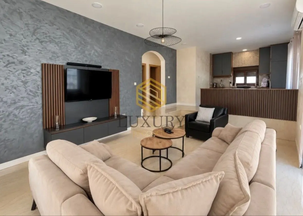 Modern living room with a sofa set, TV, and view of the kitchen.