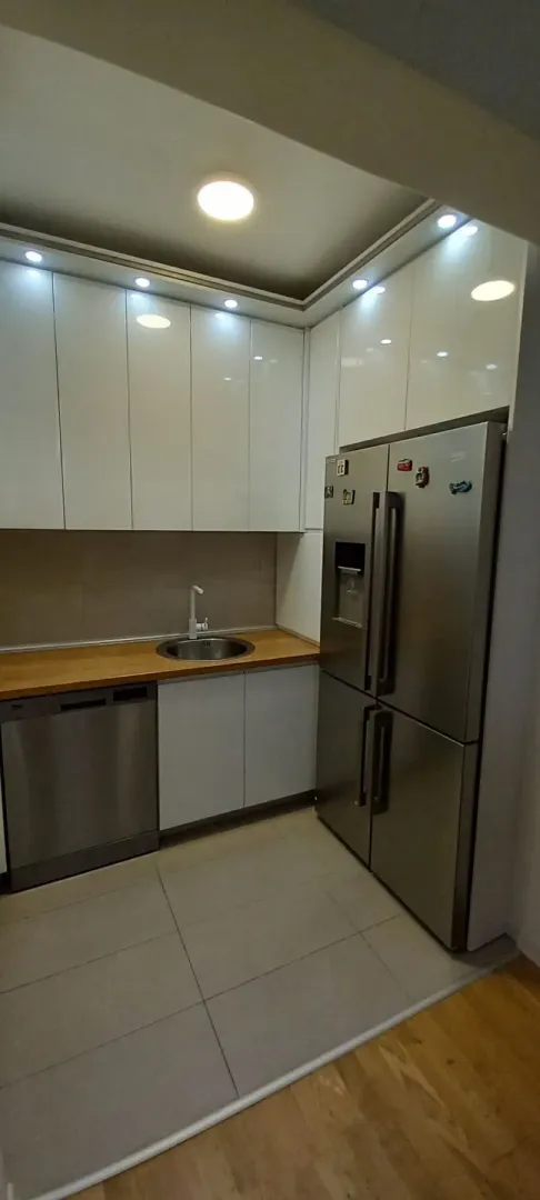 Modern kitchen with white cabinets, wooden countertop, and a large refrigerator.