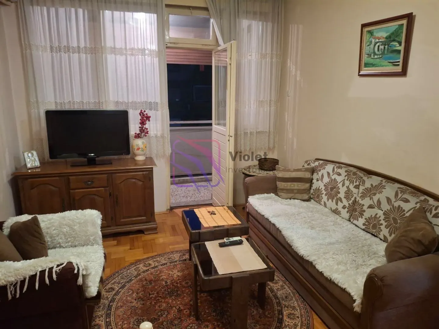 Dnevna soba sa garniturom, televizorom i izlazom na terasu.