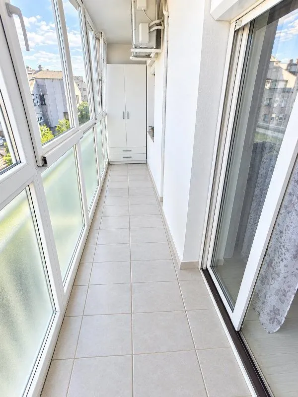 Zastakljeni balkon sa keramičkim pločicama na podu i ugradnim ormarom.