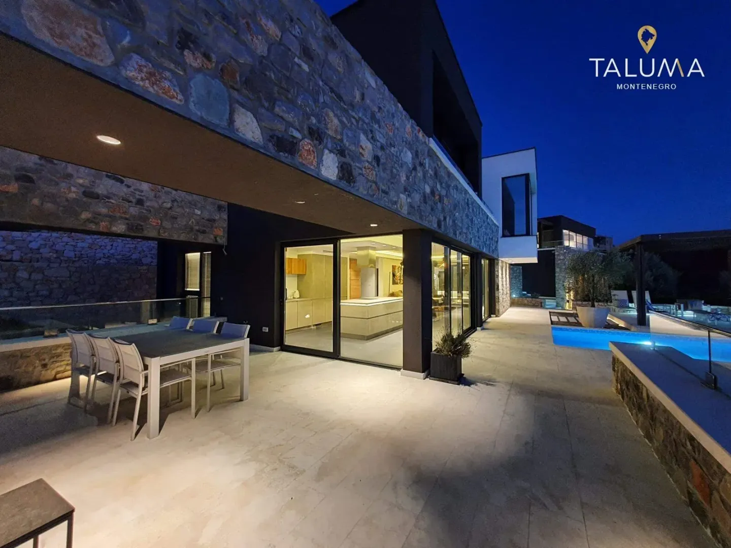 Exterior of the villa at night with a dining table, terrace, and swimming pool.