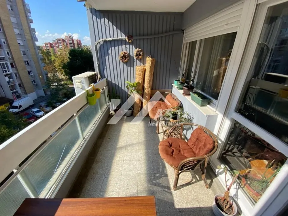 Namešten balkon sa garniturom za sedenje i pogledom na okolne zgrade.