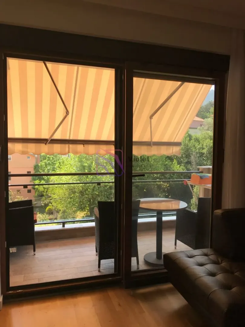 Pogled kroz balkonska vrata na terasu sa garniturom za sjedenje i tendom.