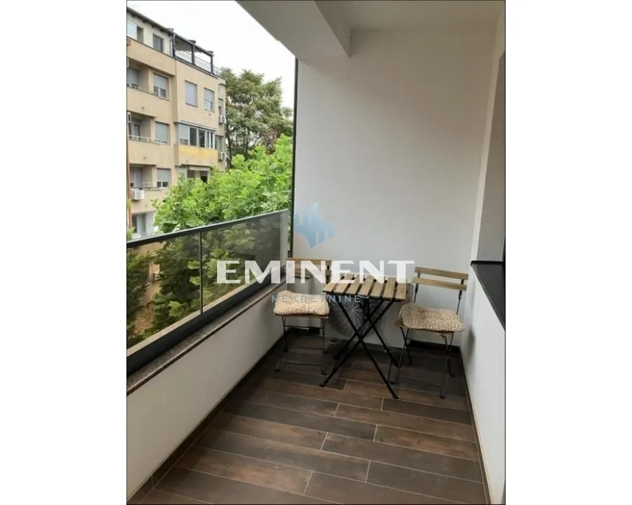 Natkriveni balkon sa garniturom za sedenje i pogledom na okolne zgrade.