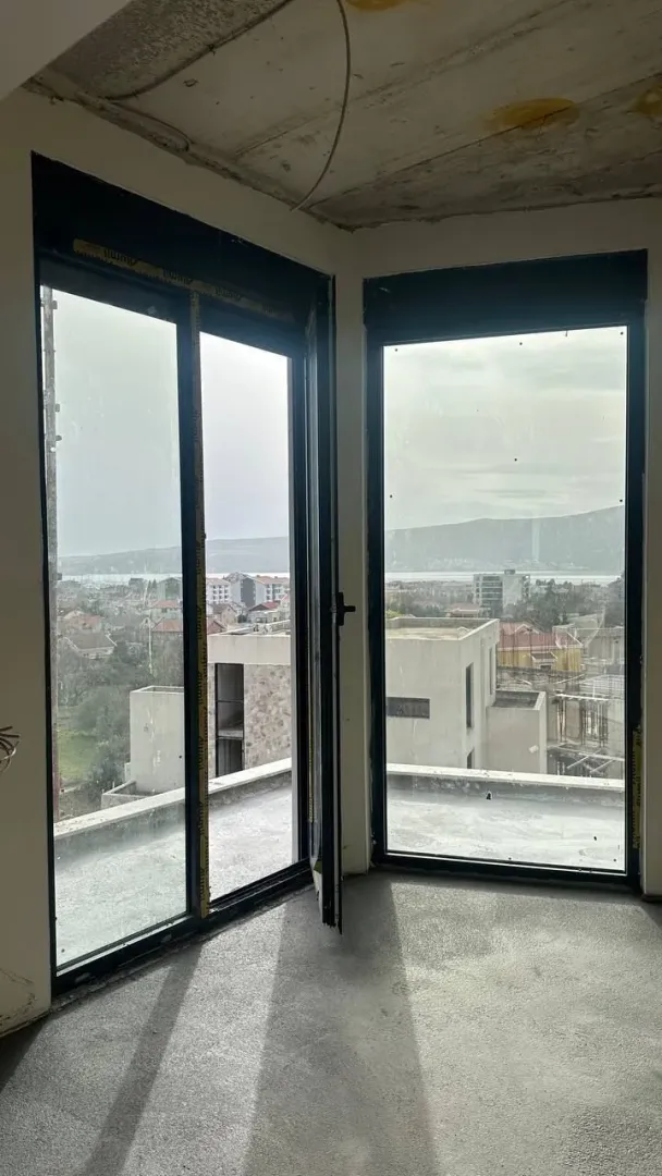 Nepreuređena prostorija u izgradnji sa velikim prozorima i pogledom na okolinu.