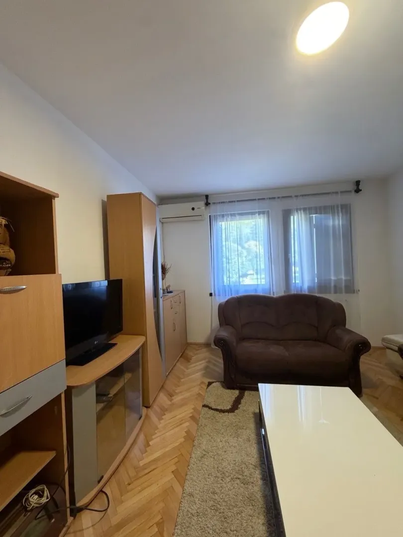 Dnevna soba sa garniturom, TV-om i drvenim namještajem.