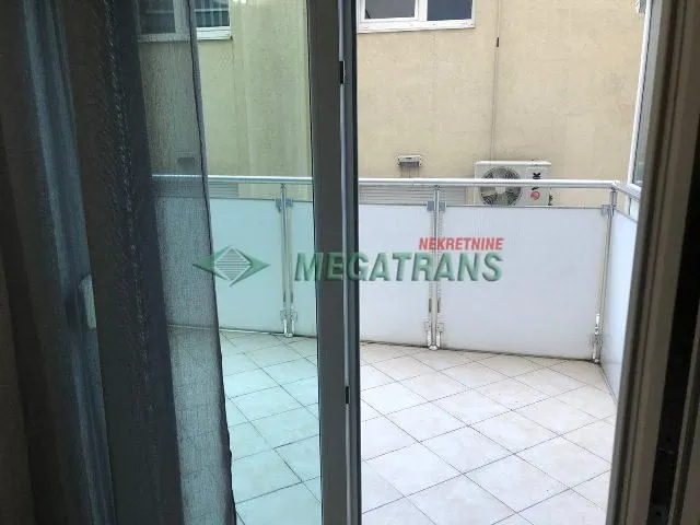 Pogled na popločanu terasu sa staklenom ogradom kroz balkonska vrata.