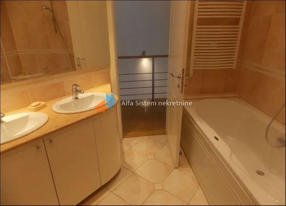 Bathroom with a bathtub, two washbasins and beige tiles.