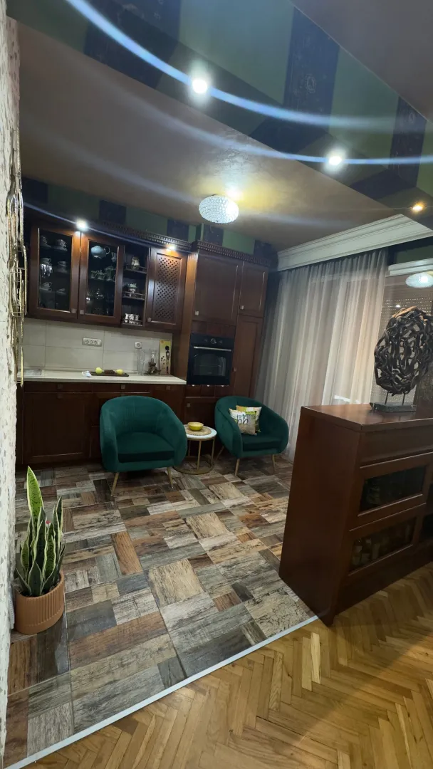Kuhinja u tamnim drvenim tonovima sa dva zelena fotelja i šarenim keramičkim pločicama na podu.