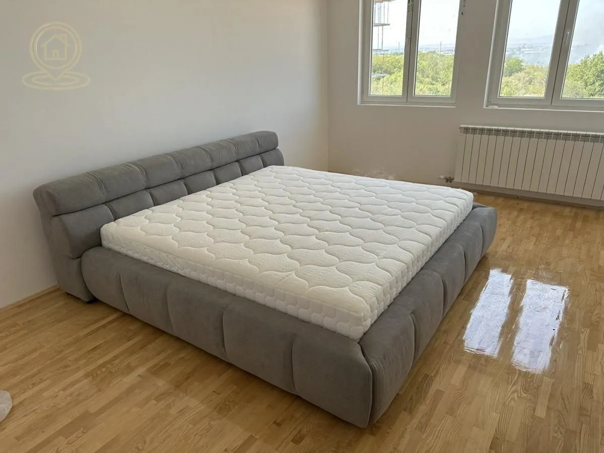 A bedroom with a large upholstered bed and hardwood flooring.