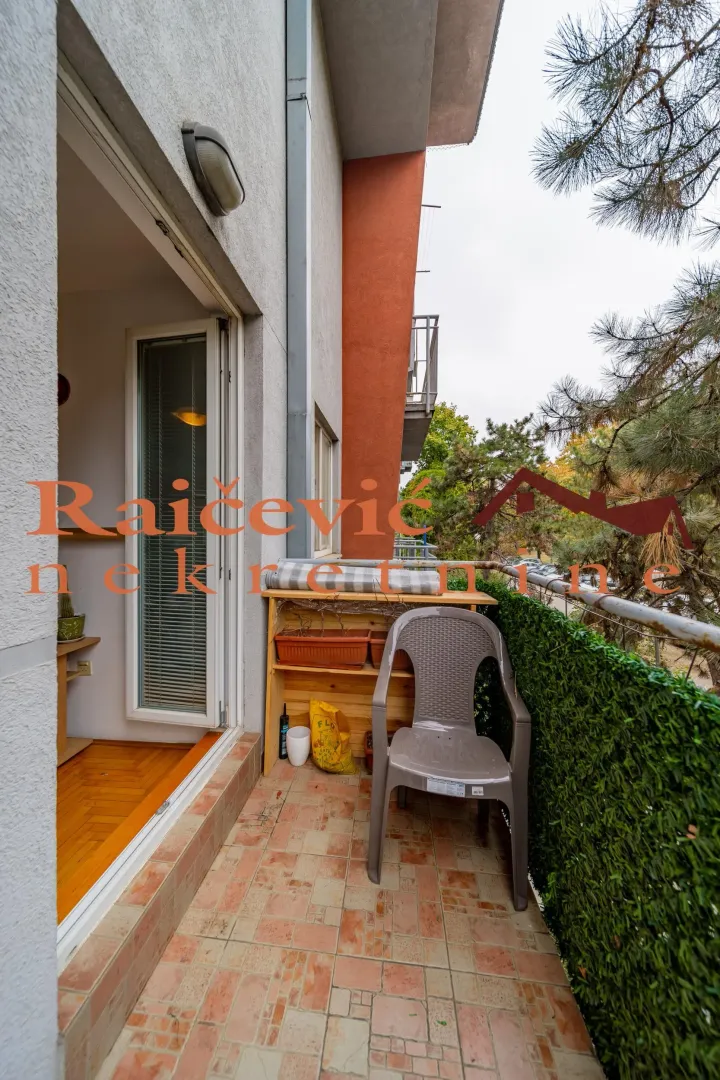 Small tiled balcony with a chair and a view of greenery.