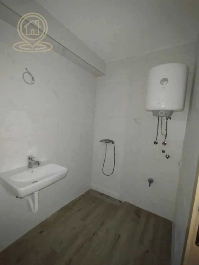 Kupatilo obloženo svetlim pločicama sa umivaonikom i bojlerom.