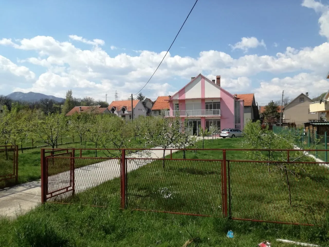 Dvospratna kuća sa roze fasadom i prostranim dvorištem okruženim ogradom.