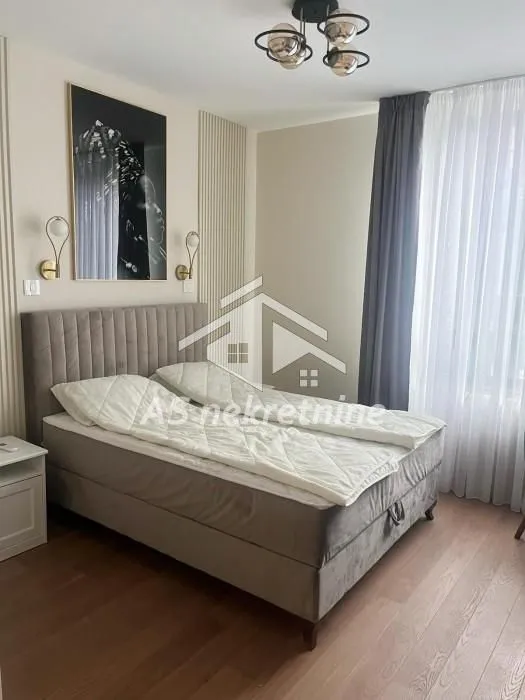 Furnished bedroom with a double bed, artwork on the wall, and a window with curtains.