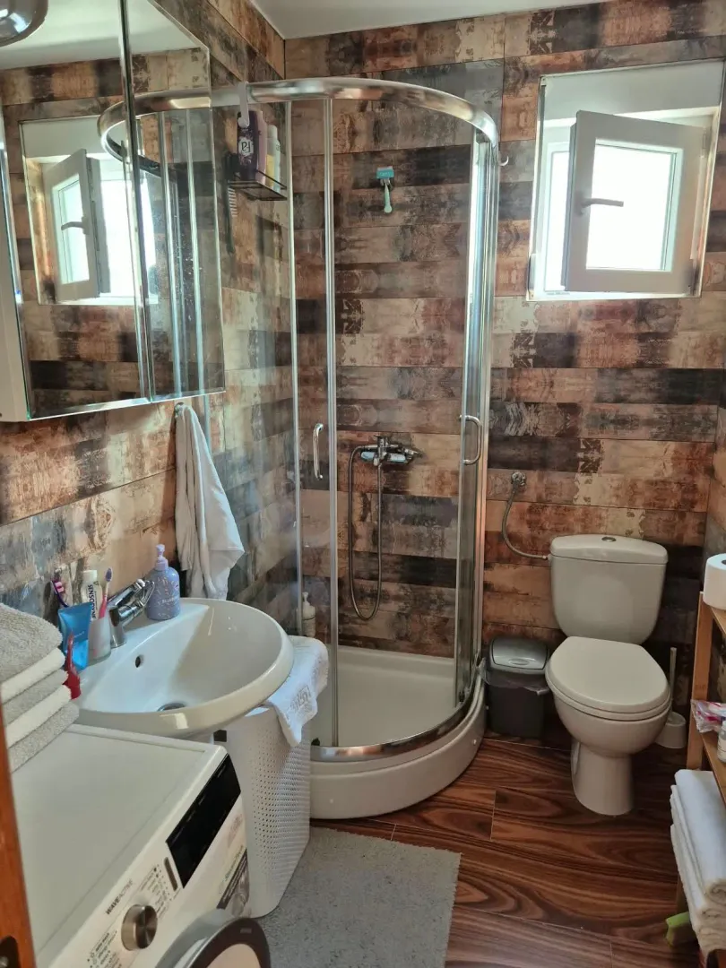 Small bathroom with a shower cabin, washbasin, toilet, and washing machine.