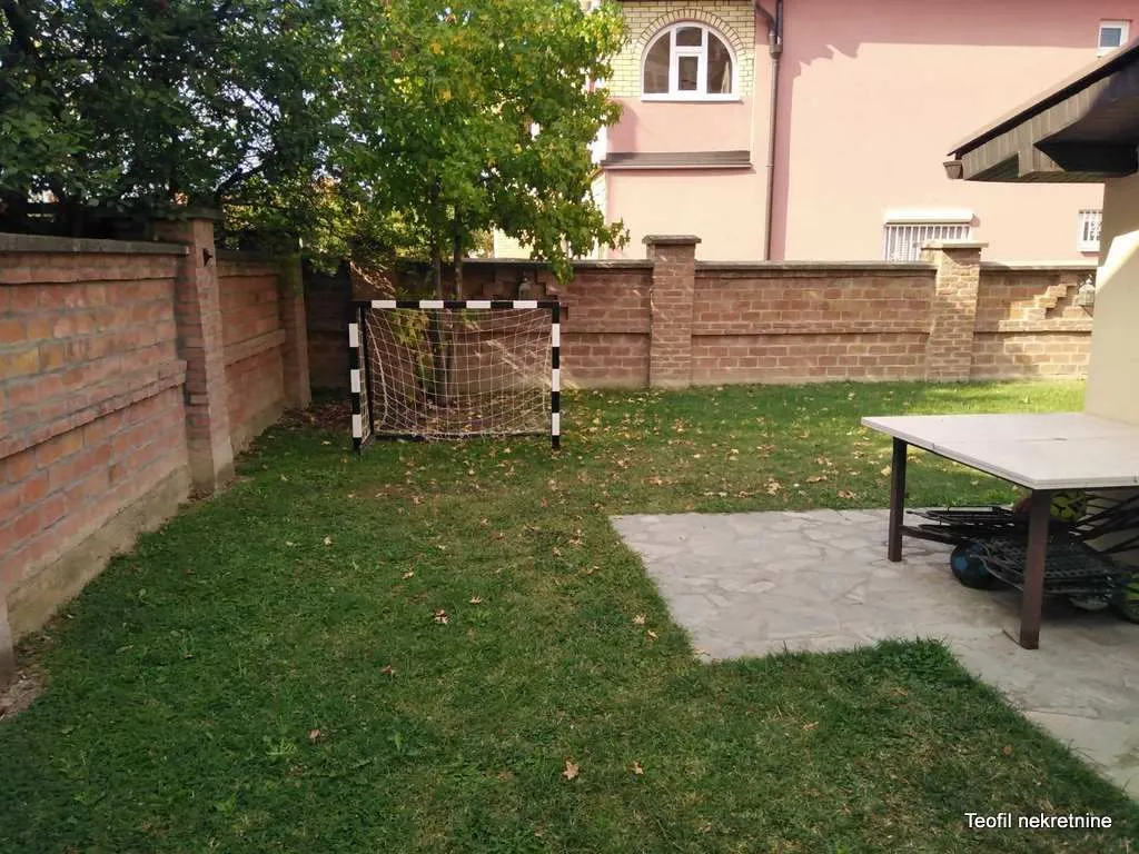 Dvorište kuće sa travnjakom, zidanim ogradnim zidom i malim golom za fudbal.