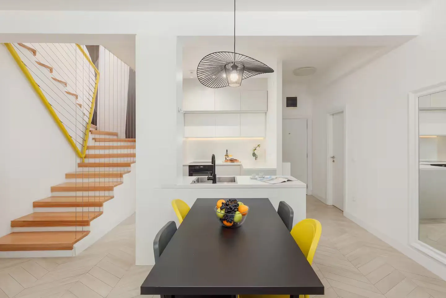 Dining area with a modern kitchen and stairs in the background.