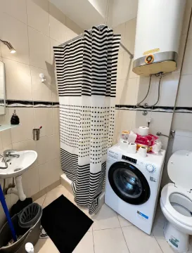 Kupatilo opremljeno tuš kabinom sa crno-belom zavesom, umivaonikom, veš mašinom i toaletom. - image 11