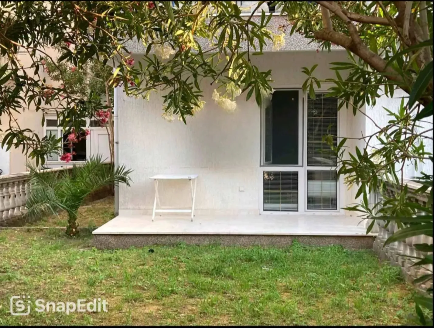 Pogled na terasu i dvorište kuće okružene zelenilom.
