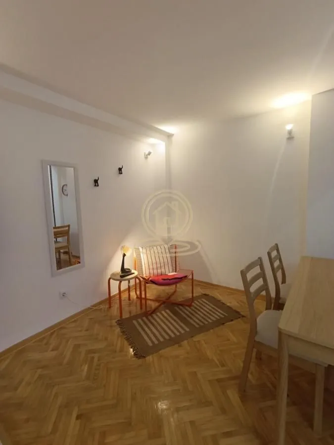 Dnevna soba sa drvenim parketom, foteljom i trpezarijskim stolom.