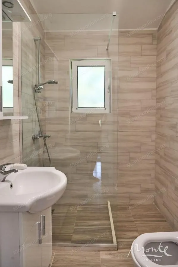 Moderne kupatilo sa tuš kabinom, umivaonikom i pločicama u dezenu drveta.