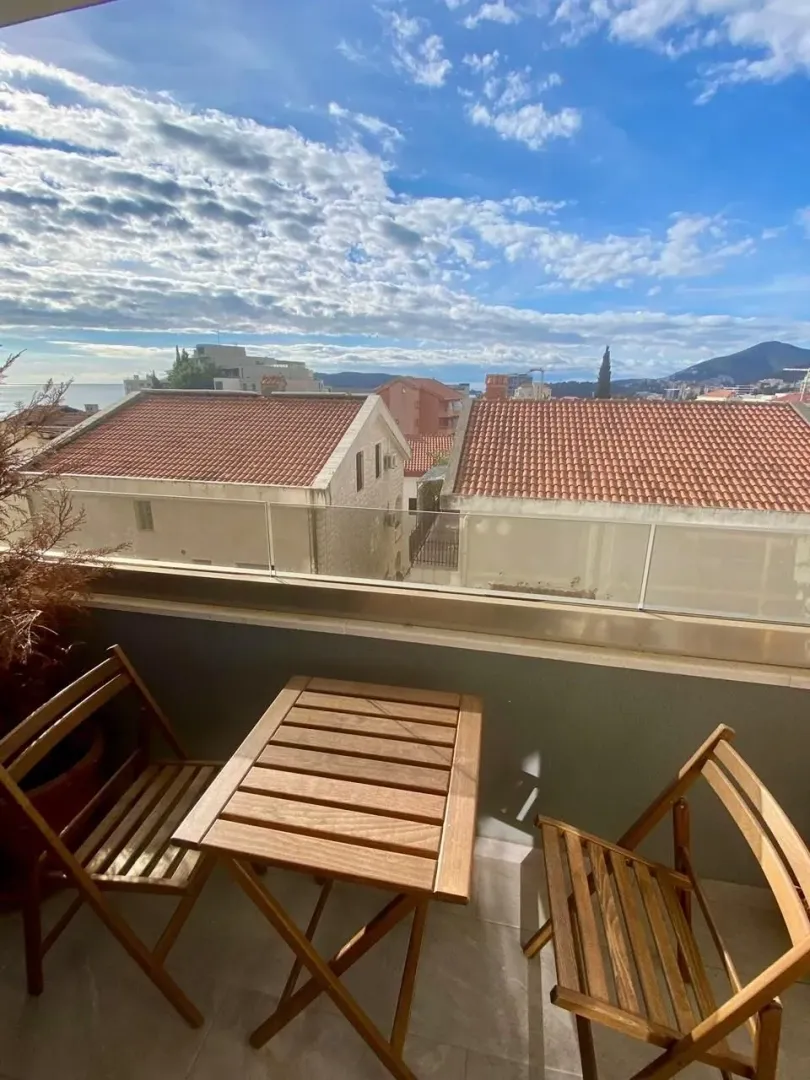 Furnished balcony with a wooden table and chairs and a view of surrounding buildings and the sky.