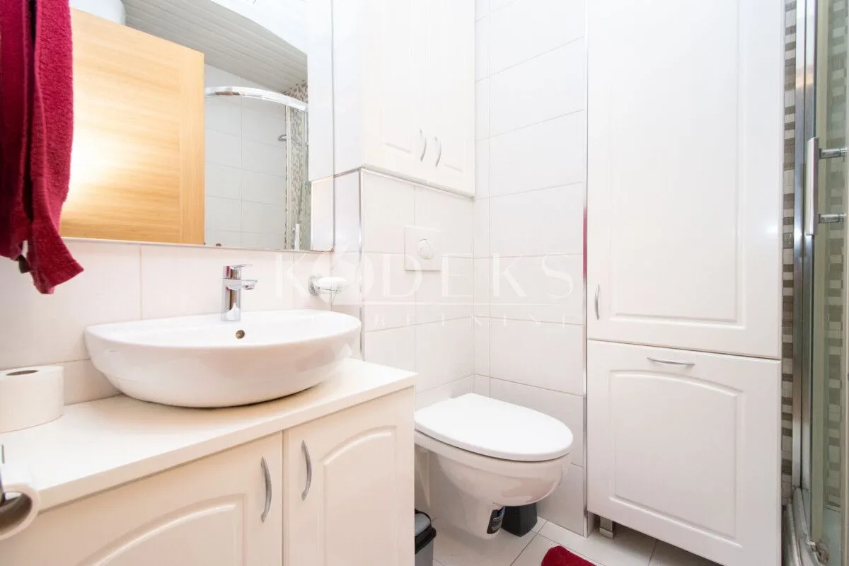 A well-lit bathroom with a washbasin, toilet, cabinet, and mirror.